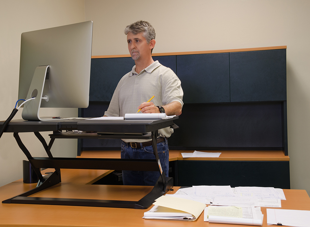 Man standing at his sit-stand desk working at computer